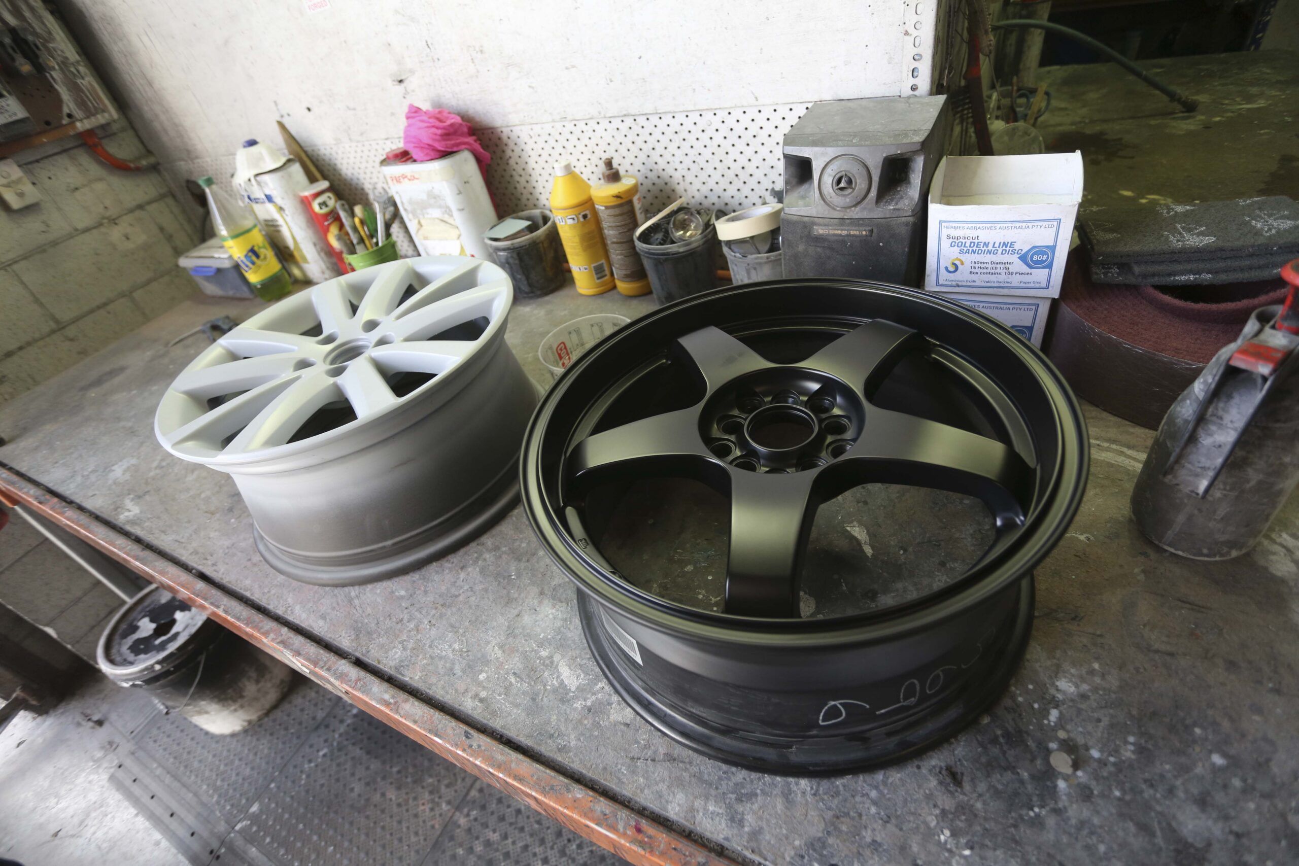 A grey-primed wheel beside a freshly finished matte black wheel, showing the transformation
